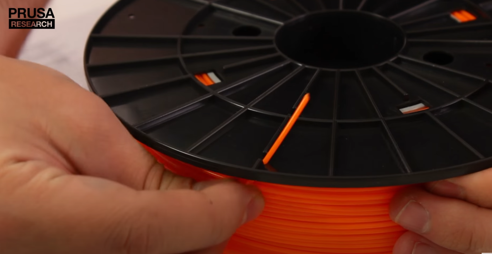 Picture of someone pushing orange filament through hole on the side of filament spool